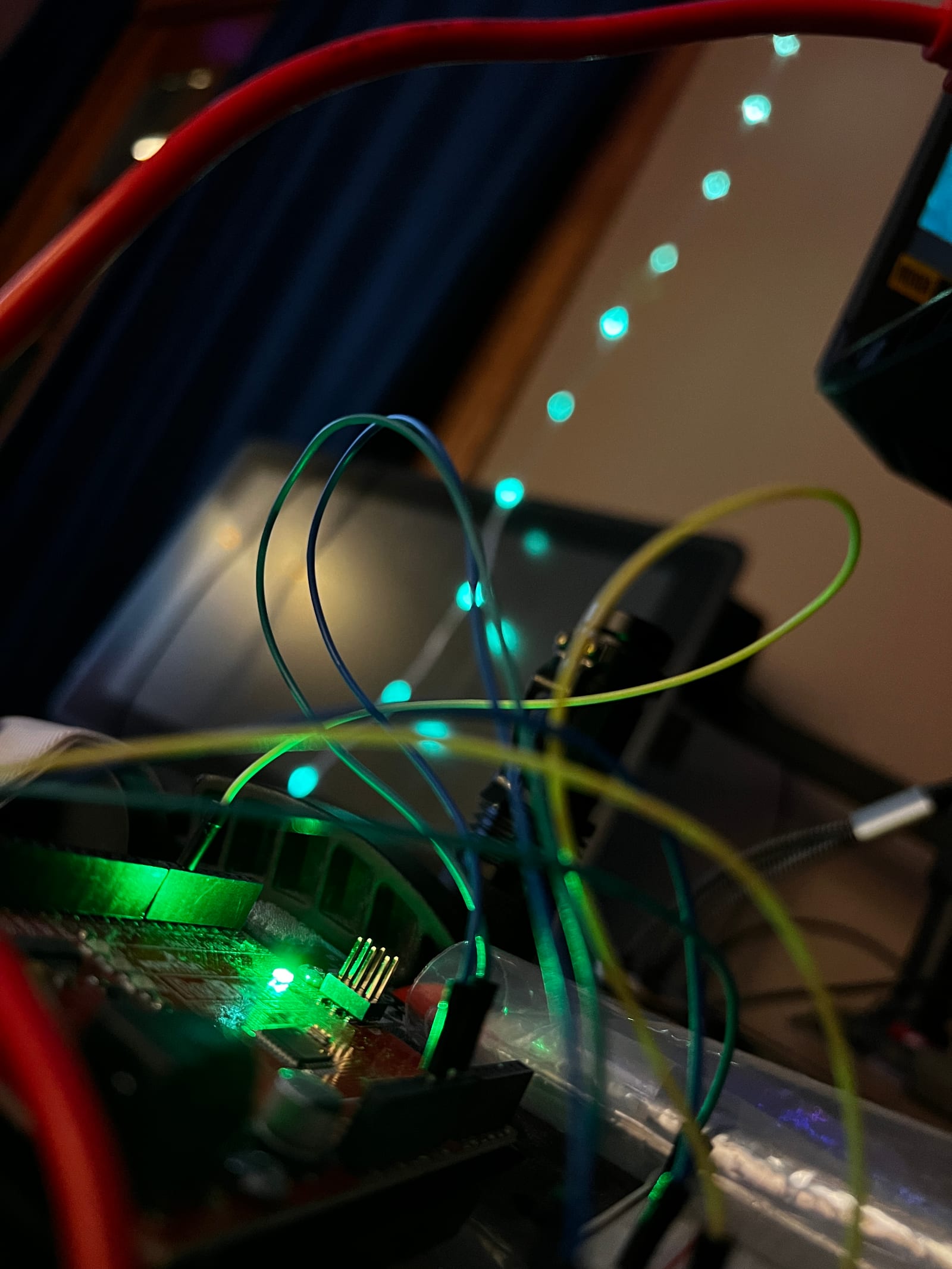 A microcontroller and looping wires mid-build, addressable LEDs glowing teal on the wall behind