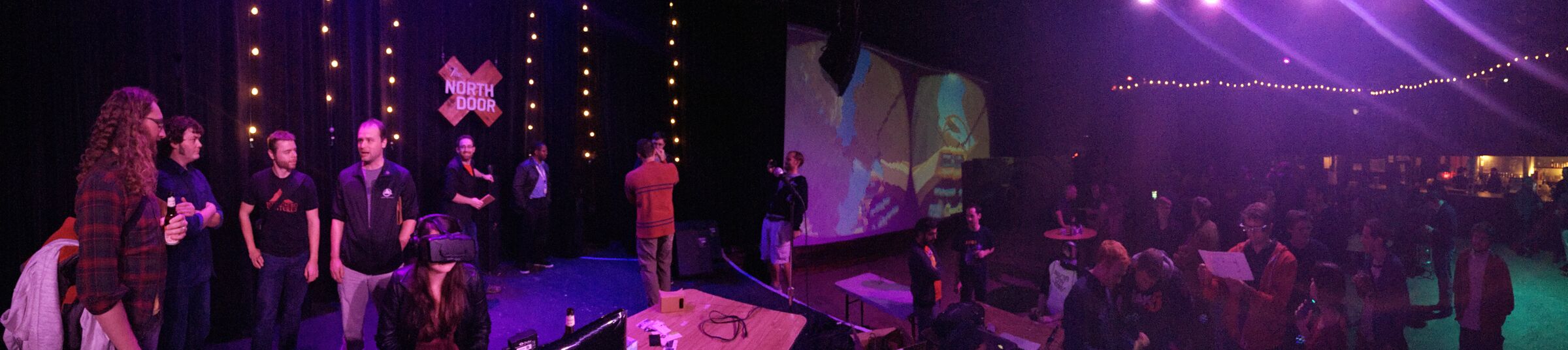 A wide panoramic photo of the 2014 Austin VR meetup at The North Door, with PolyFish projected on a large screen while attendees watch