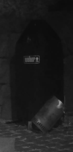 Infrared trail-camera crop of a covered Weber barbecue against a stone wall, the word weber legible on the lid.